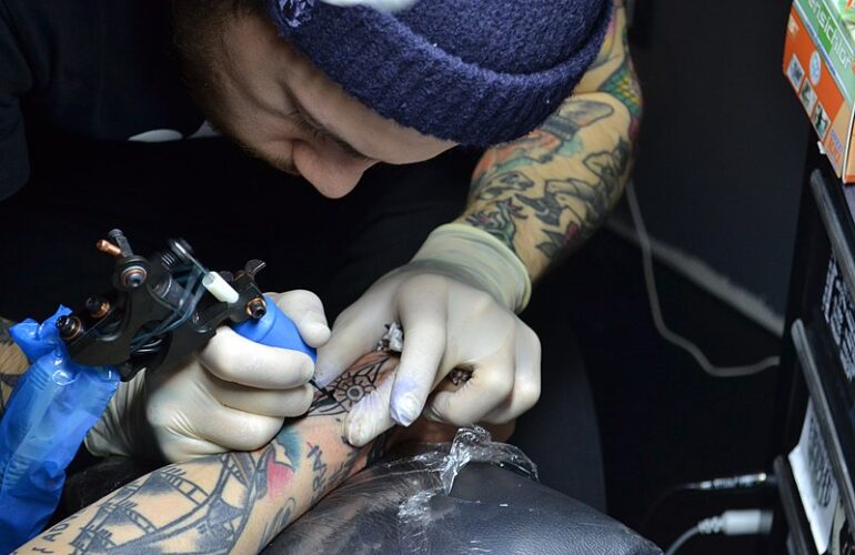 a tattoo artist with green tattoos doing an arm tattoo